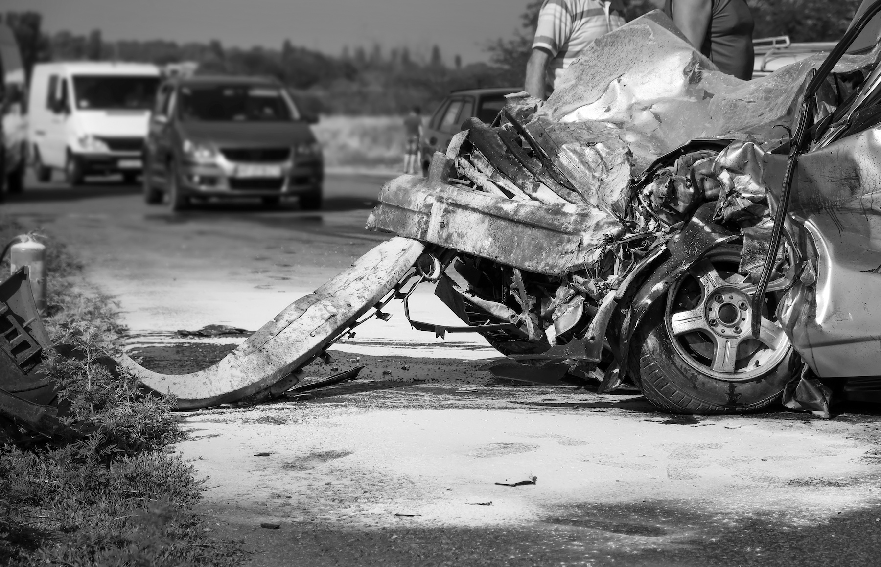 Black and white photo of a severe car crash scene with a heavily damaged vehicle in the foreground and other cars stopped in the background. This image, perfect for a blog archive on personal injury, starkly captures the aftermath of the collision. Lancaster, CA Car Accident Attorneys